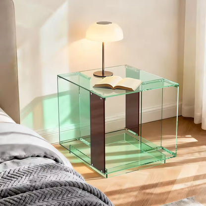 2-tier green tinted acrylic end table next to a bed, topped with a modern lamp and open book.