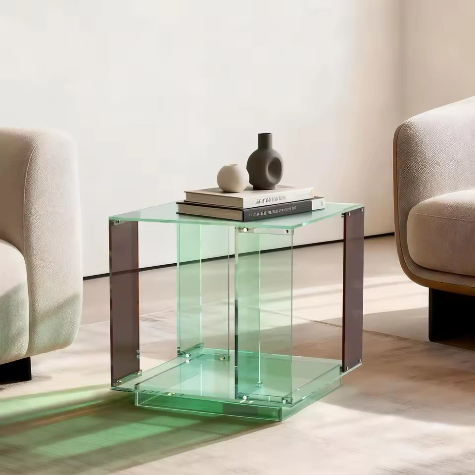 Two-tier green-tinted acrylic end table with books and small decorative vases, set between chairs.