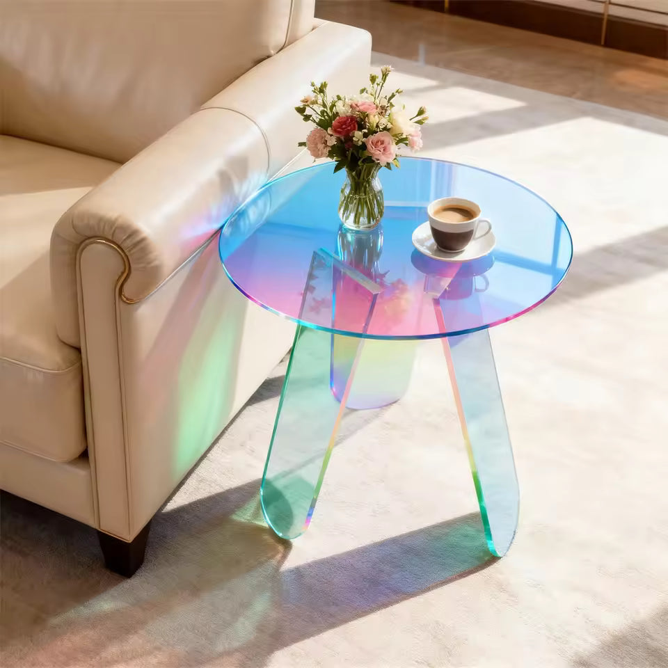 Round iridescent acrylic side table holding a vase of flowers and coffee next to a sofa.