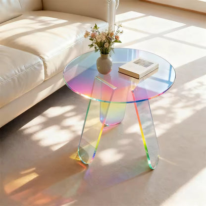Round iridescent acrylic side table holding a vase and book, placed next to a white leather sofa.