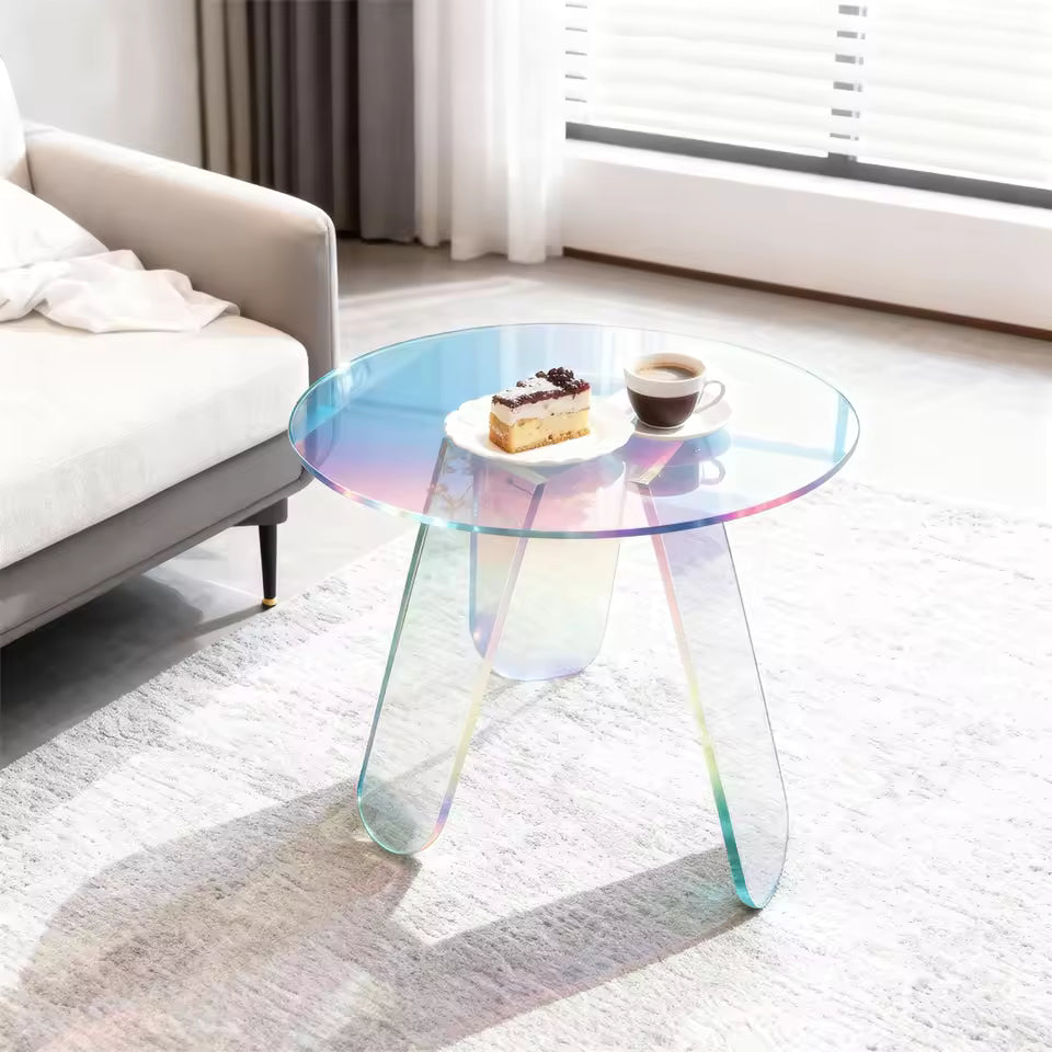 Round iridescent acrylic side table holding cake and coffee next to a sofa in a bright room.