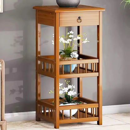 Tall bamboo plant stand end table with a top drawer and two open shelves displaying potted flowers.