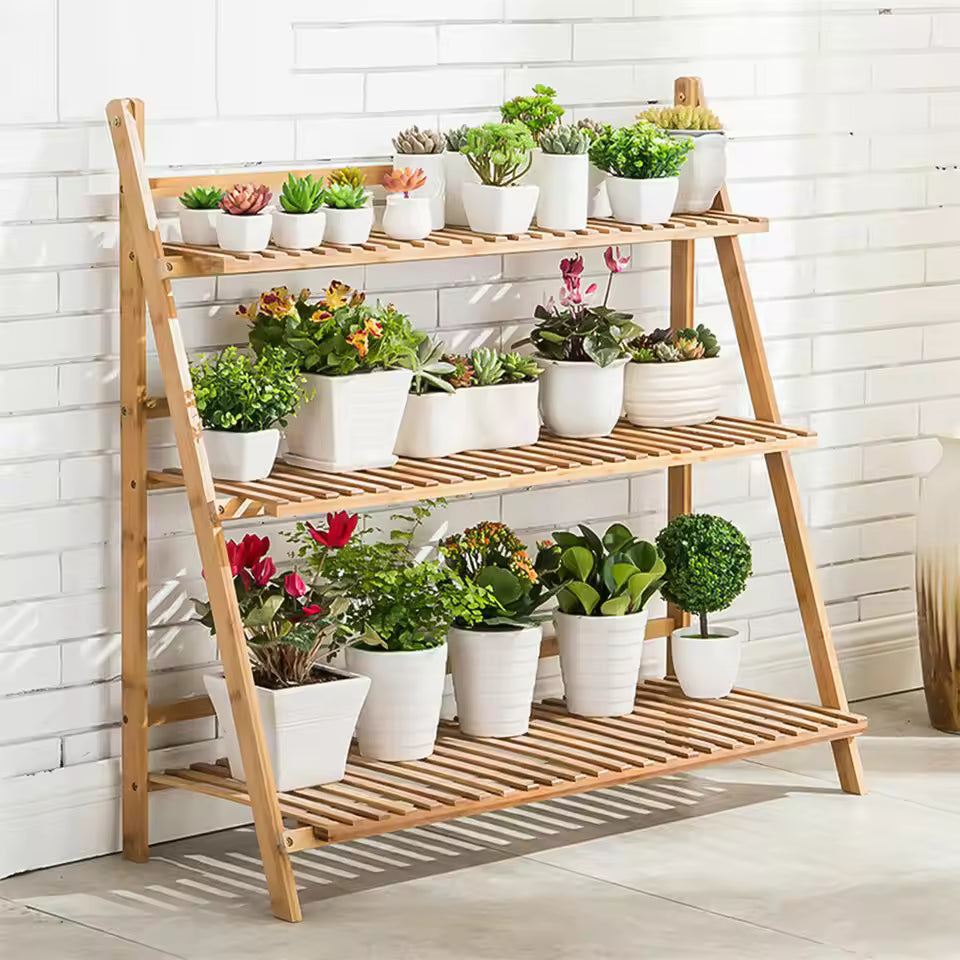 3-tier wooden ladder plant stand holding various potted plants against a white brick wall.