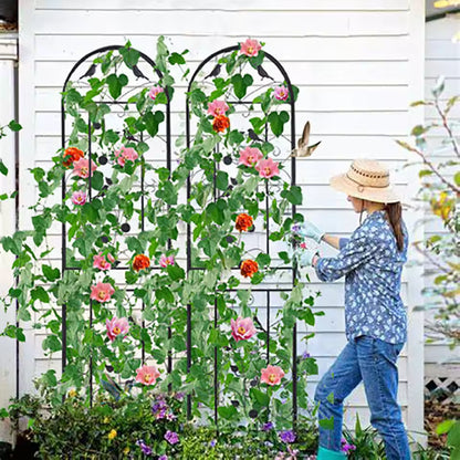 Two tall arched black metal garden trellises with climbing pink flowers and a gardener tending to them.