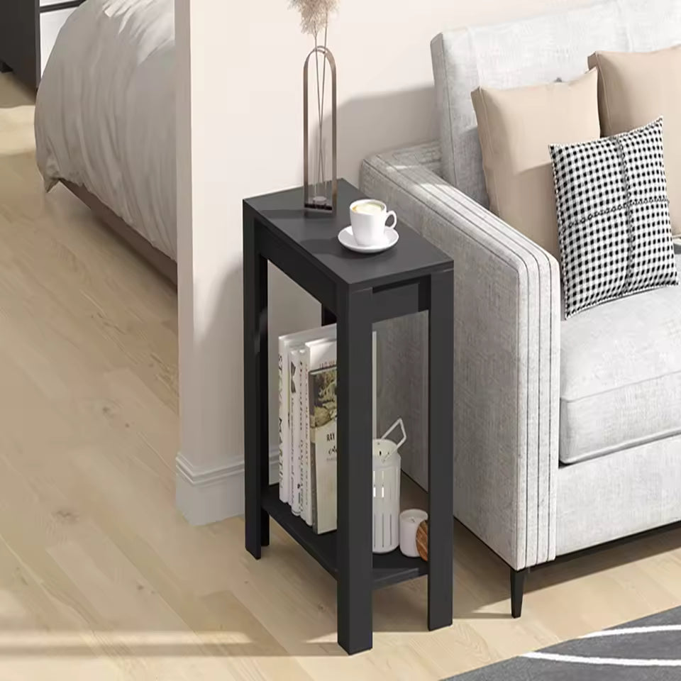 Narrow modern black end table with 2-tier storage, placed beside a grey sofa holding books and coffee.