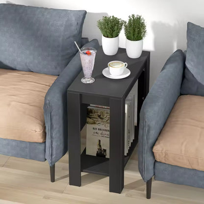 Narrow black side table with two tiers, holding drinks and potted plants, set between two armchairs.