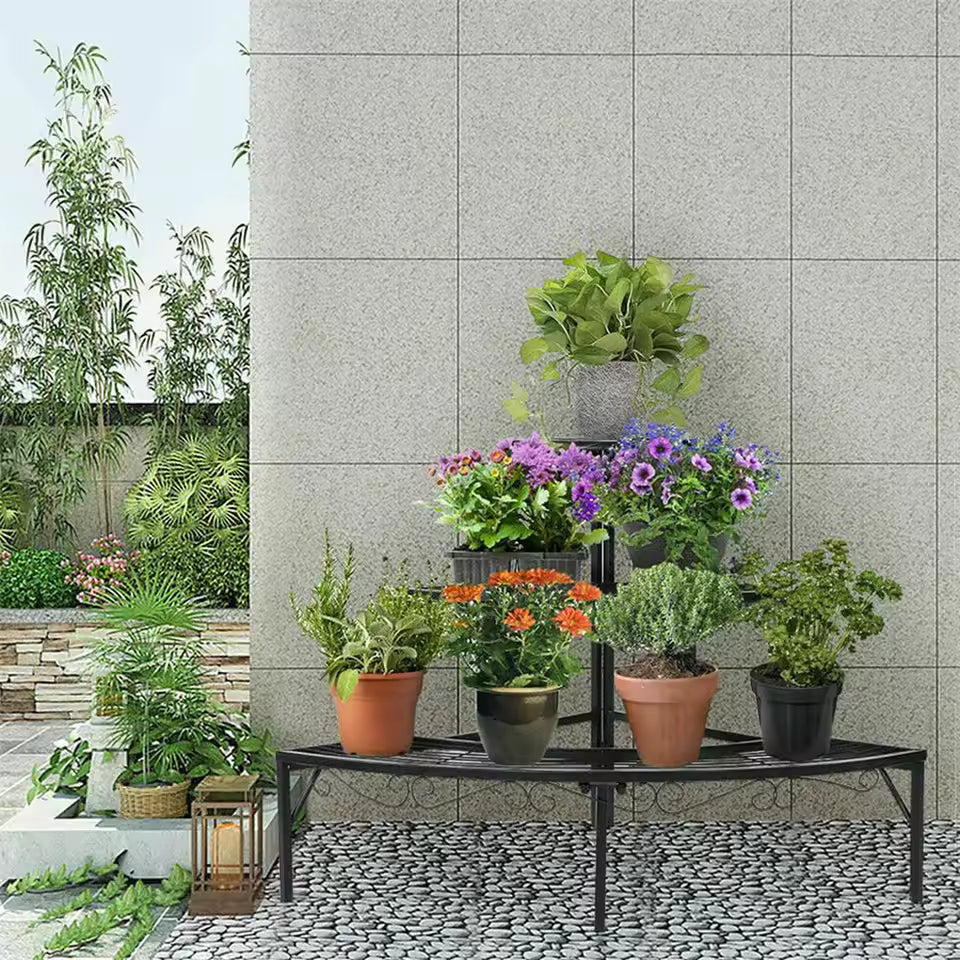 Three-tier black metal corner plant stand holding potted flowers and plants on a patio.