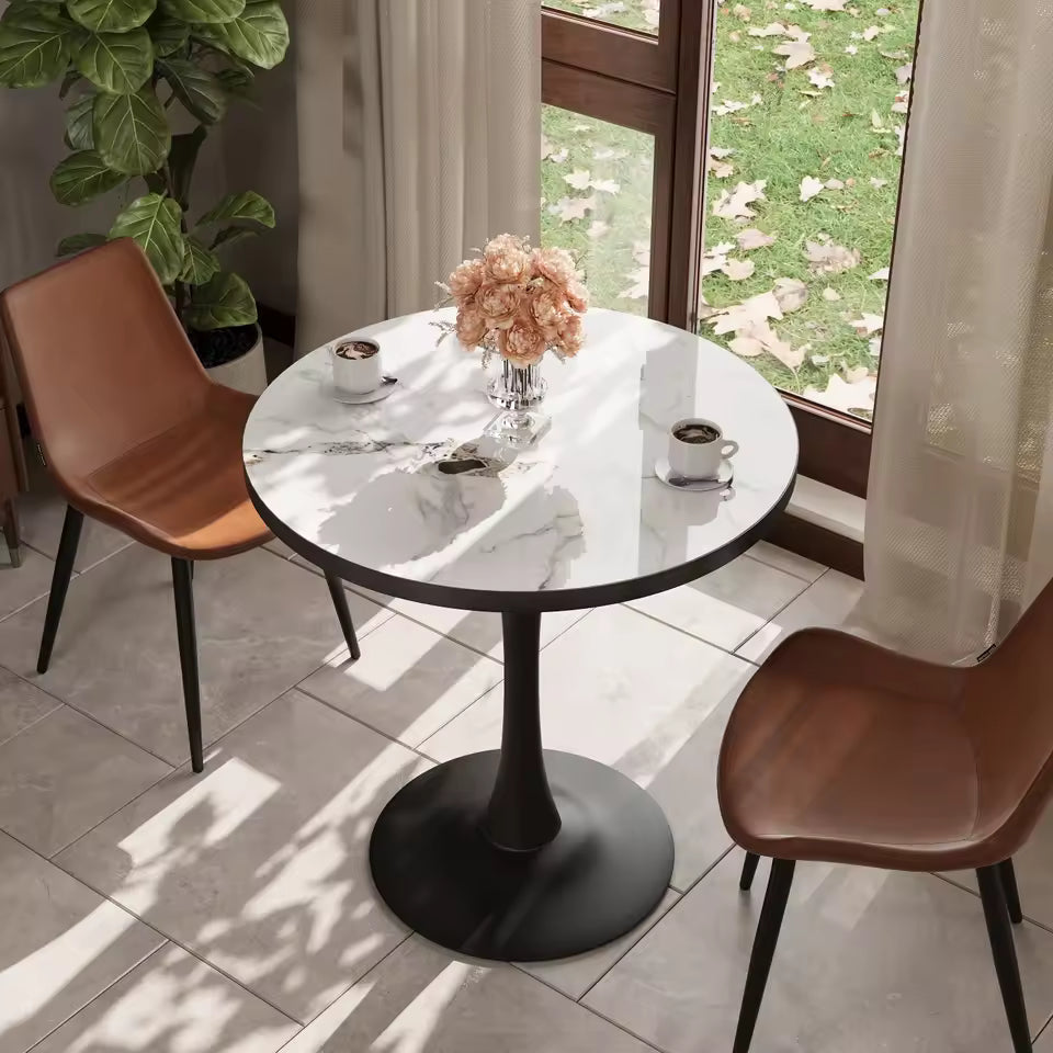 Round marble-top dining table with a black tulip base, set between two brown leather chairs near a window.