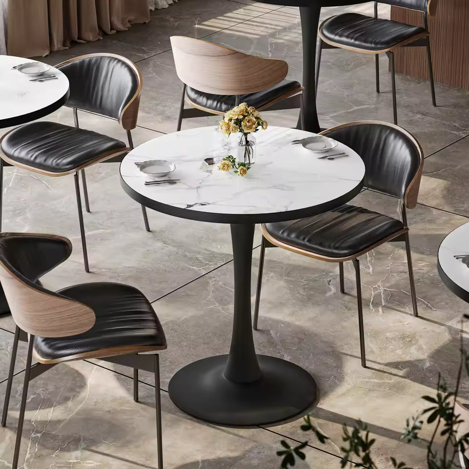 Round white marble pedestal dining table with yellow flowers, surrounded by modern black chairs.
