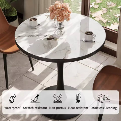 Round white marble-look bistro table with a black pedestal base set next to a sunny window.