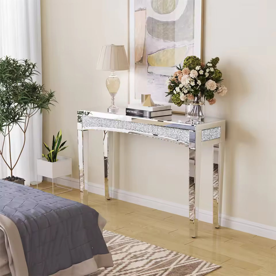 Silver mirrored console table with crushed diamond trim, topped with a lamp and vase of flowers.