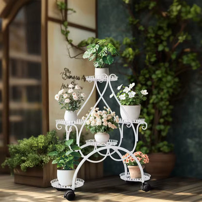 White 6-tier metal plant stand on wheels displaying various potted flowers and green plants indoors.