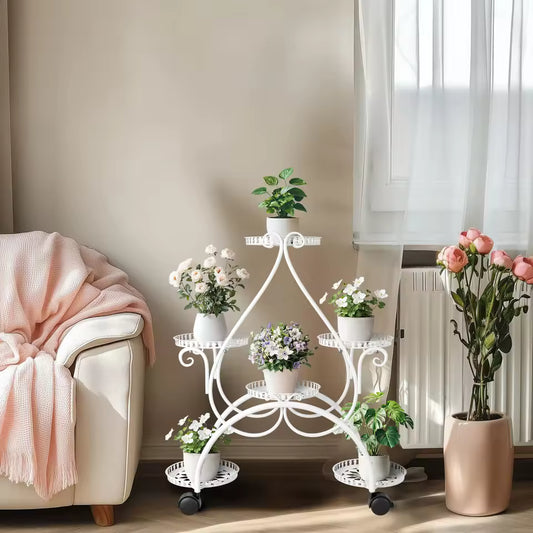 White multi-tier metal plant stand on wheels displaying potted flowers in a living room.