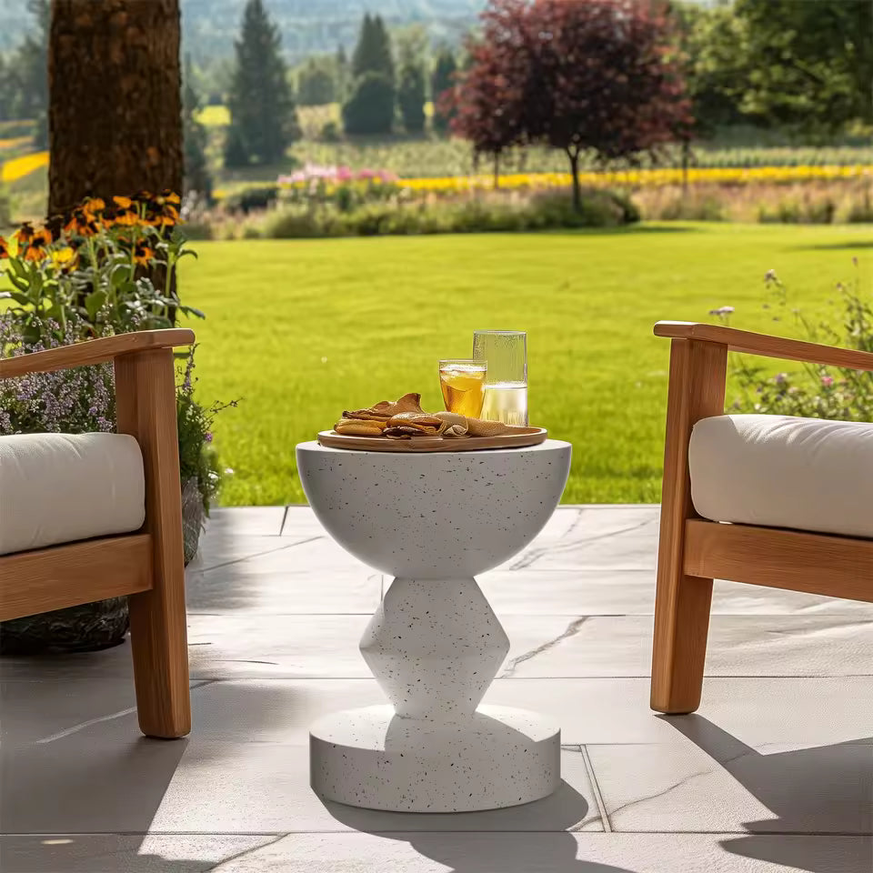 White speckled concrete side table holding drinks and snacks between two wooden patio chairs.