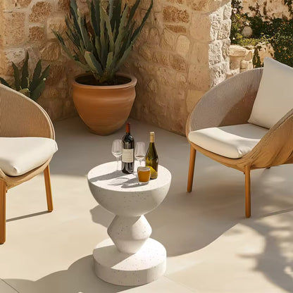 White sculpted concrete accent side table on a patio, holding wine bottles, glasses, and a drink.