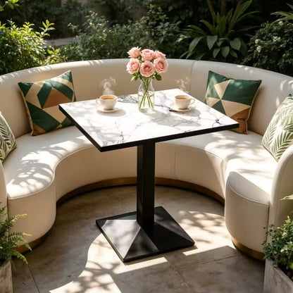 Square faux-marble top pedestal table with coffee cups and roses, surrounded by a curved booth.