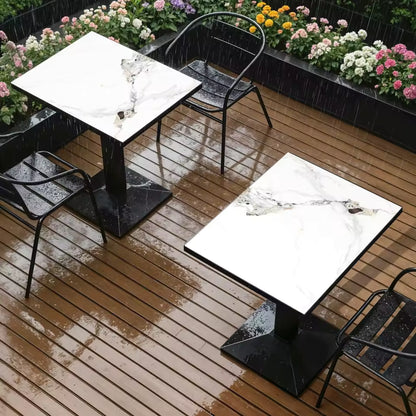 White marble-look rectangular bistro tables with black pedestal bases on a wet wooden deck.