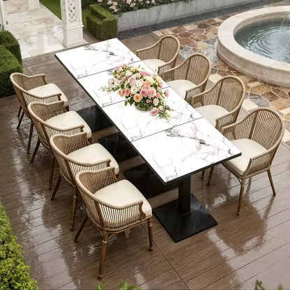White marble-top outdoor dining table with woven armchairs on a patio next to a fountain.