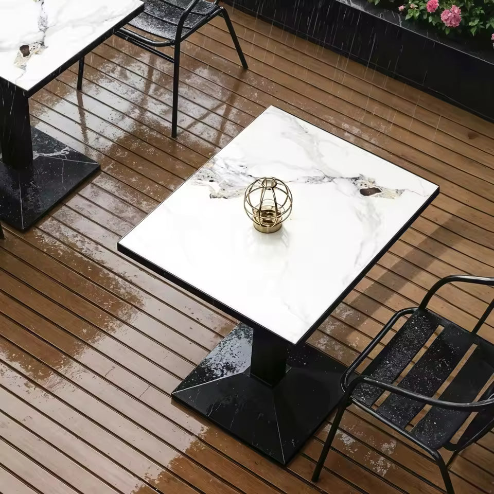 White marble-top bistro table with a black pedestal base on a wet wooden patio deck.