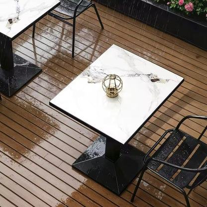 White marble-top bistro table with a black pedestal base on a wet wooden patio deck.