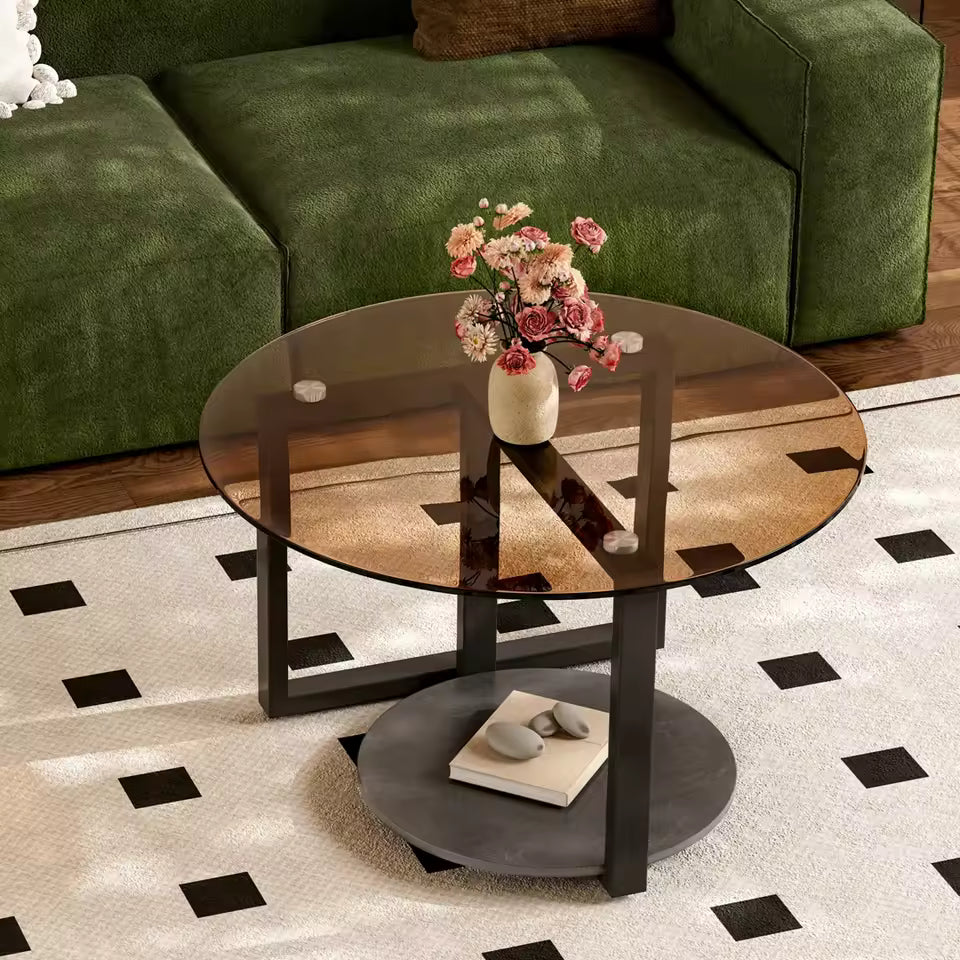 Round amber glass coffee table with a black metal frame, lower grey shelf, and pink flowers on top.