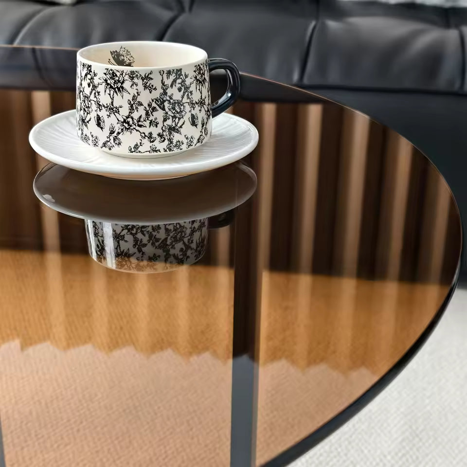 Black and white patterned teacup on a white saucer, resting on an amber-tinted glass table top.