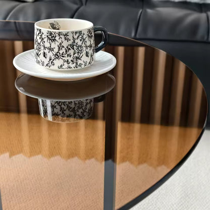Black and white patterned teacup on a white saucer, resting on an amber-tinted glass table top.