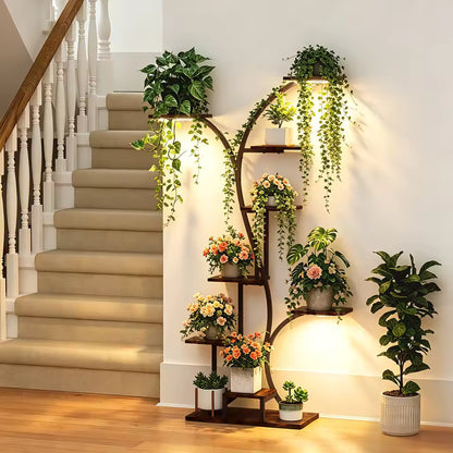Curved multi-tiered plant stand with grow lights displaying potted plants and flowers by a staircase.