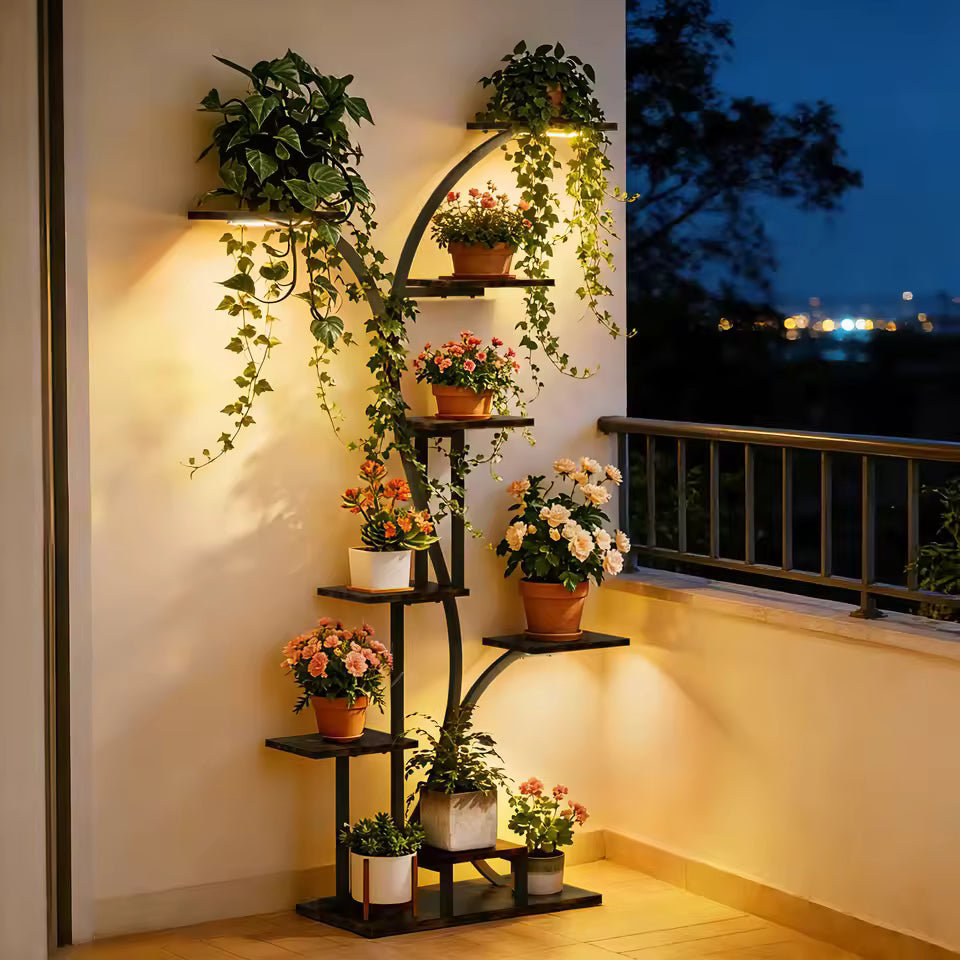 Tall curved metal plant stand with grow lights displaying potted plants on a balcony at night.