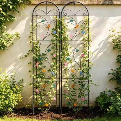 Two arched metal garden trellis panels with decorative birds, leaves, and climbing vines against a wall.