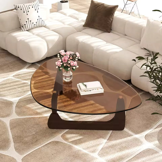 Triangular amber glass coffee table with wooden base in a modern living room next to a white sectional.