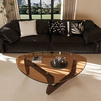 Triangular amber glass coffee table with wooden base in front of a dark leather sofa in a living room.
