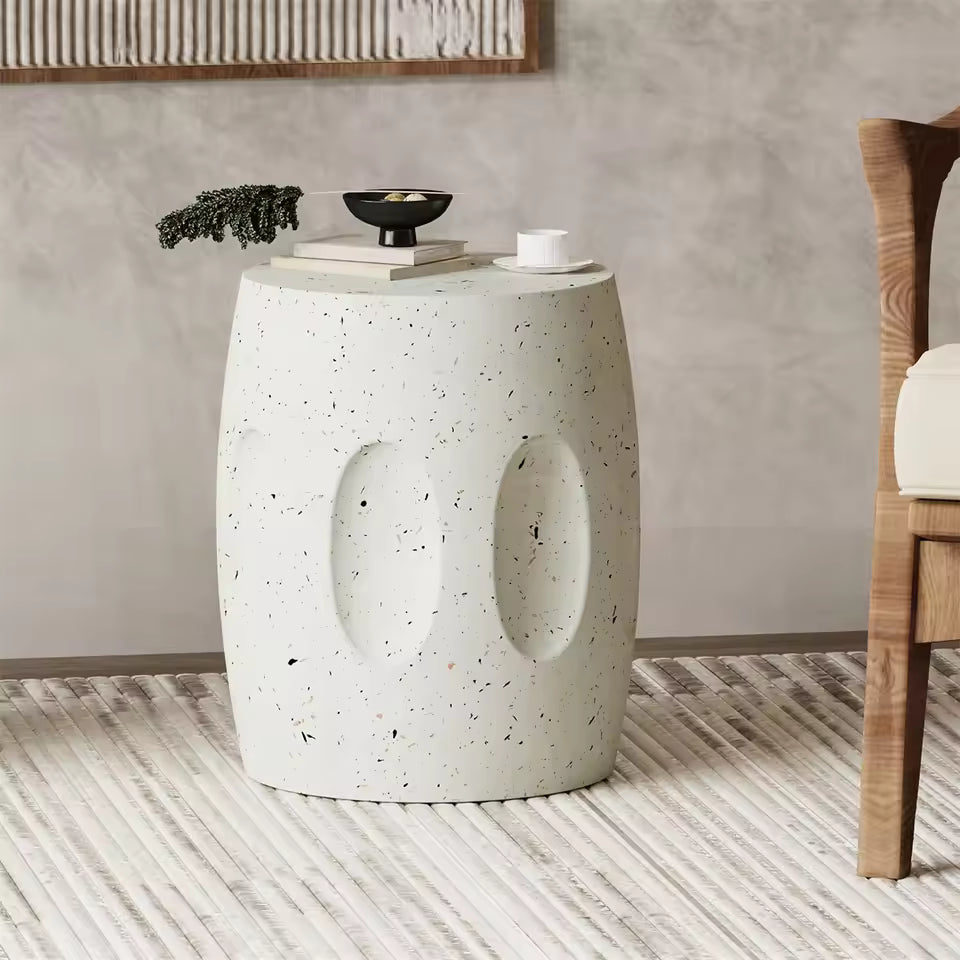 White terrazzo barrel-shaped garden stool side table with oval indentations, placed on a rug.