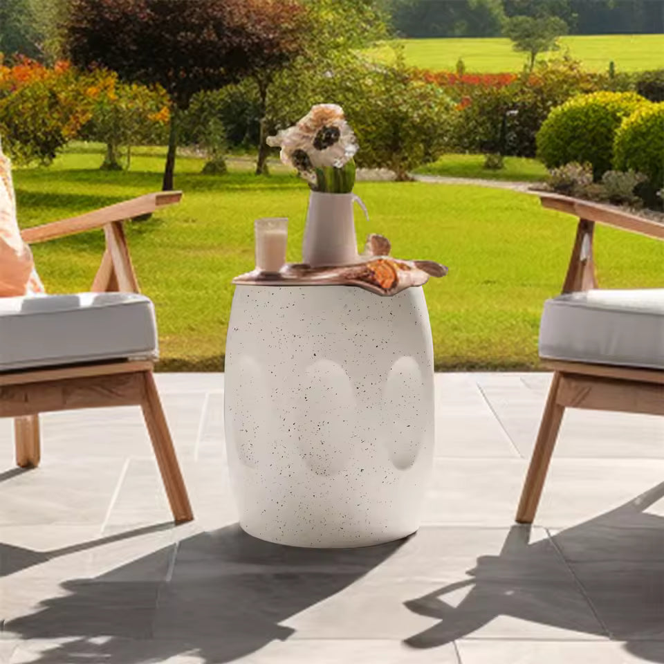 White terrazzo garden stool side table placed on a patio between two outdoor chairs.