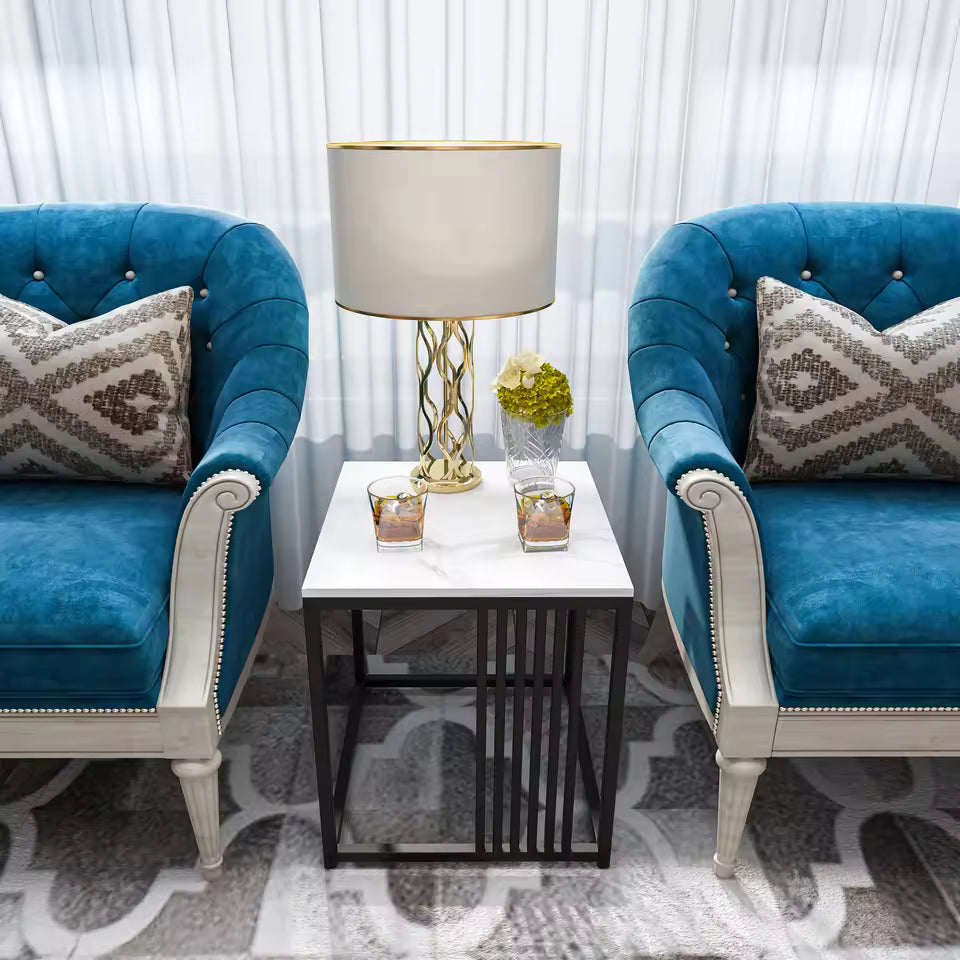 Square white marble side table with a black metal frame, set between two blue tufted armchairs.